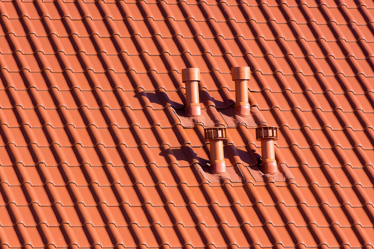 Vibrant red tiled rooftop featuring symmetrical chimneys casting soft shadows in daylight.